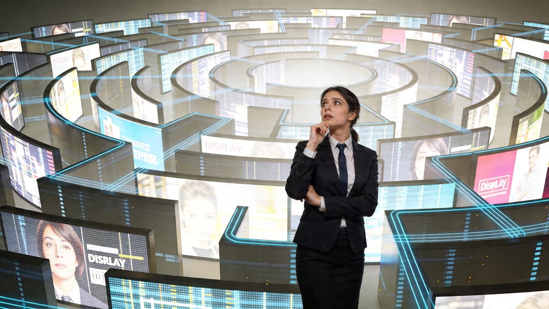 A businesswoman in a suit thinking inside a complex maze constructed of glowing digital advertising display panels.
