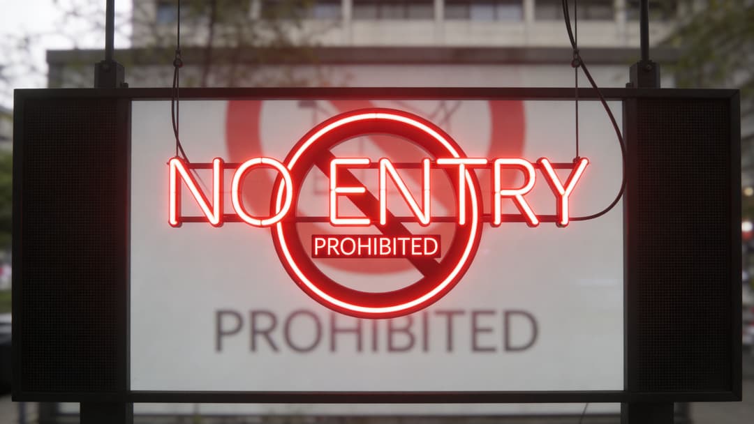A glowing red neon sign that says NO ENTRY with a prohibited symbol on a glass background.