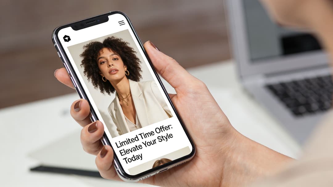 A close-up view of a person holding a smartphone showing a fashion retail advertisement on screen.